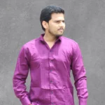 A man wearing a vibrant purple textured full-sleeve shirt, standing against a gray background.