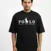 A male fashion model wearing a black oversized cotton t-shirt with a white printed polo sport chest logo and khaki trousers against a plain white background