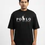 A male fashion model wearing a black oversized cotton t-shirt with a white printed polo sport chest logo and khaki trousers against a plain white background